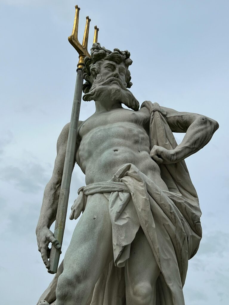 Beautiful marble statue of Neptune holding a trident, set against a cloudy sky, showcasing classical art.